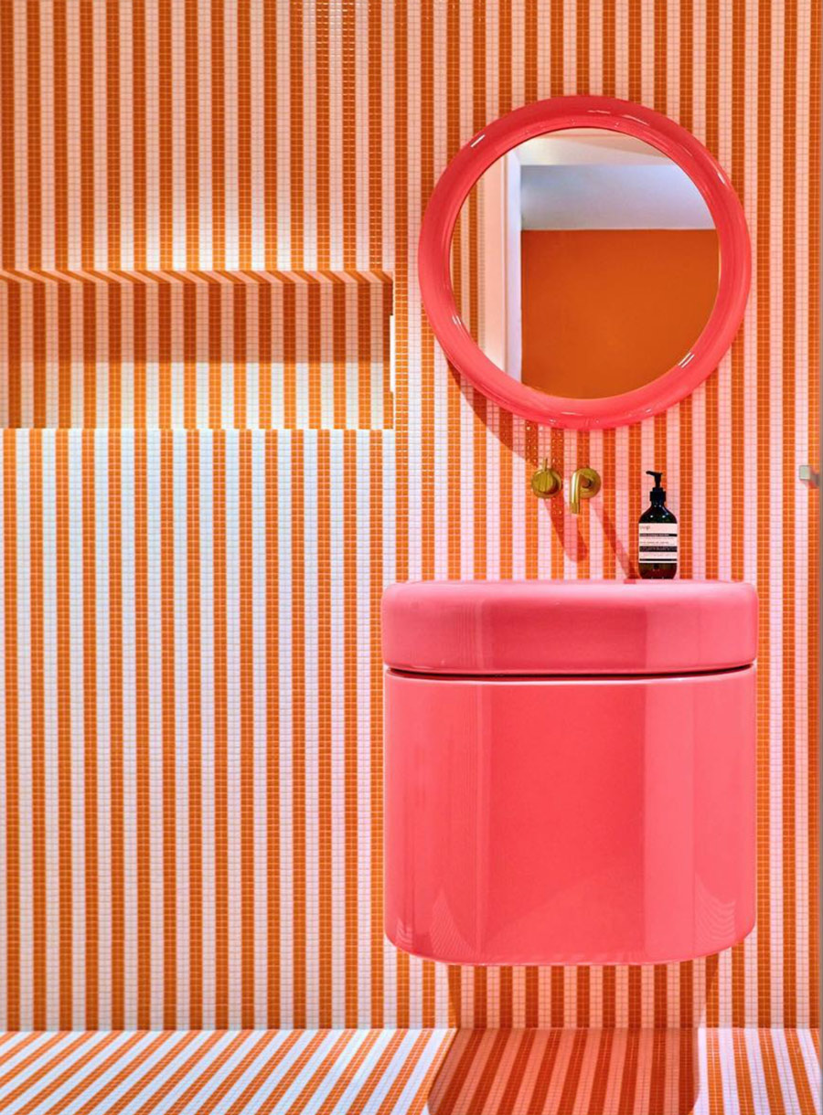 Zu sehen ist ein ausdrucksvolles Badezimmer mit einem sehr außergewöhnlichen Wand- und Bodenbelag aus Bisazza Mosaikfliesen in einem rot-weißen Streifenmuster verlegt und einem glänzend pinken Waschtisch mit passendem Spiegel.